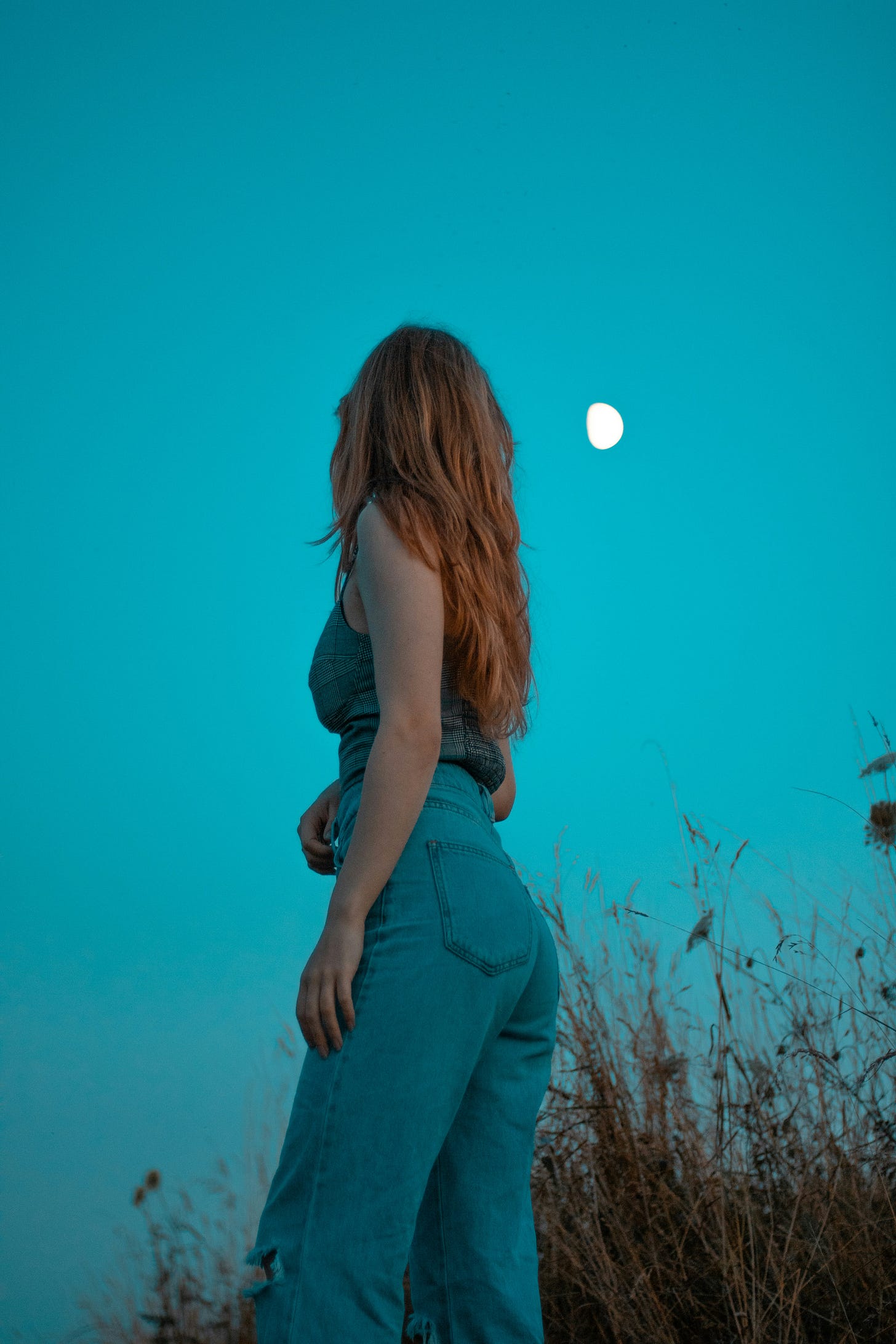  a-woman-standing-in-a-field-with-a-full-moon-in-the-background