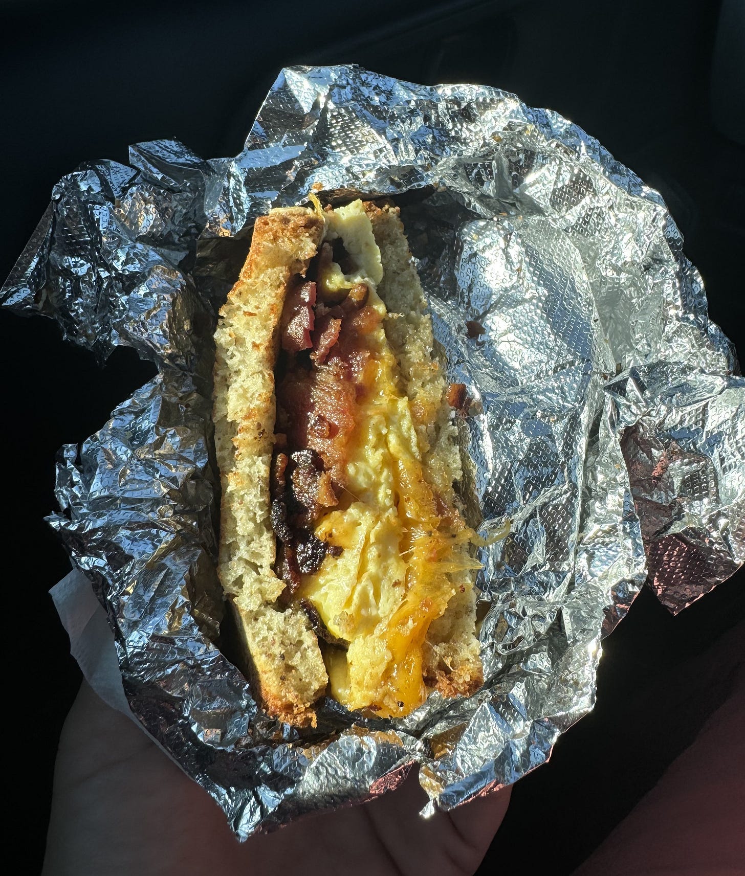 dr. sg holding half of a bacon, egg, and cheese sandwich wrapped in a piece of aluminum foil.