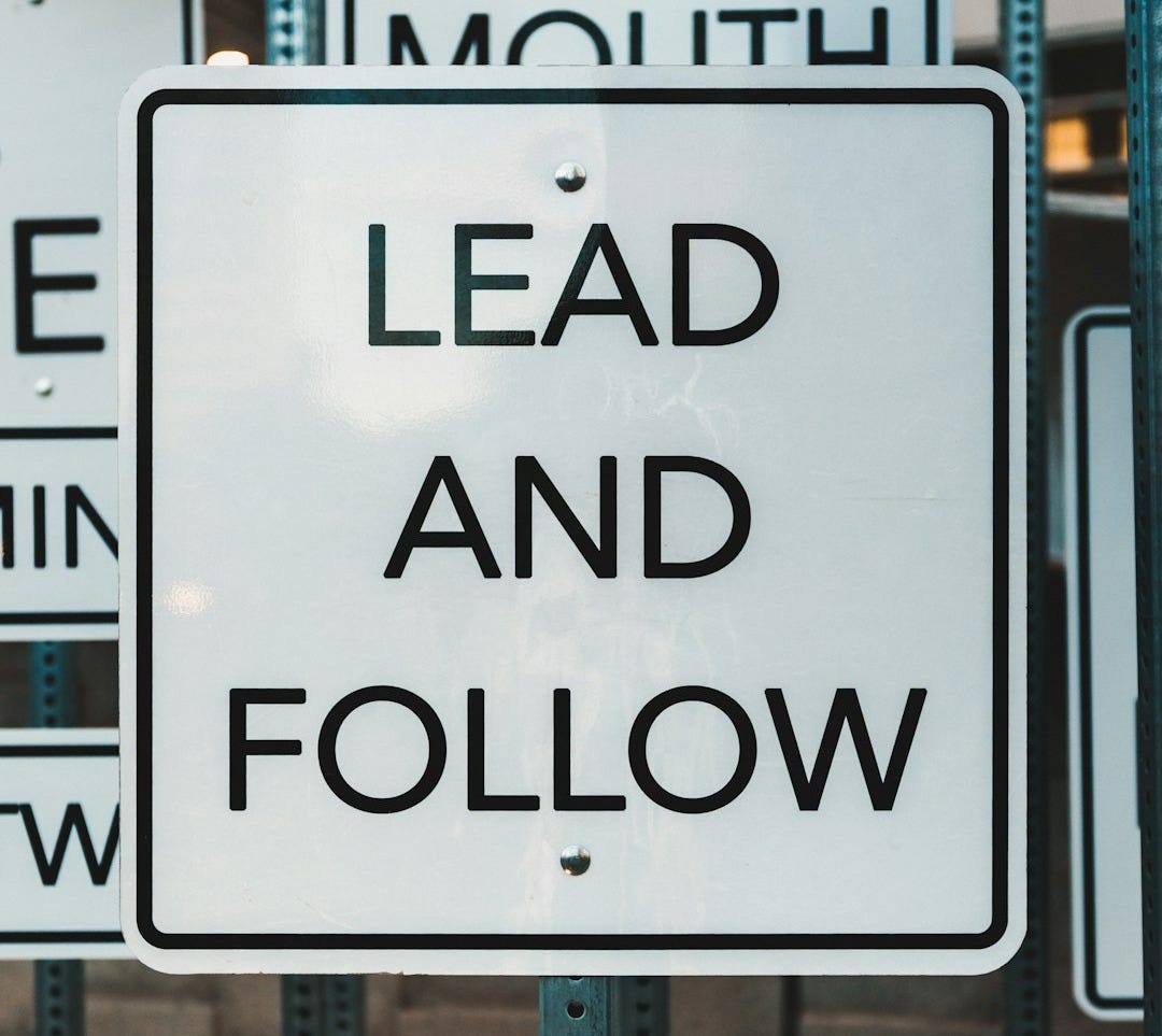 White sign with black text: lead and follow