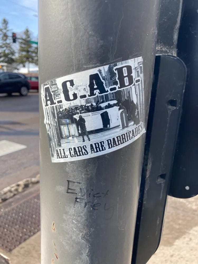 sticker on a pole at the bus stop: A.C.A.BALL CARS ARE BARRICADES