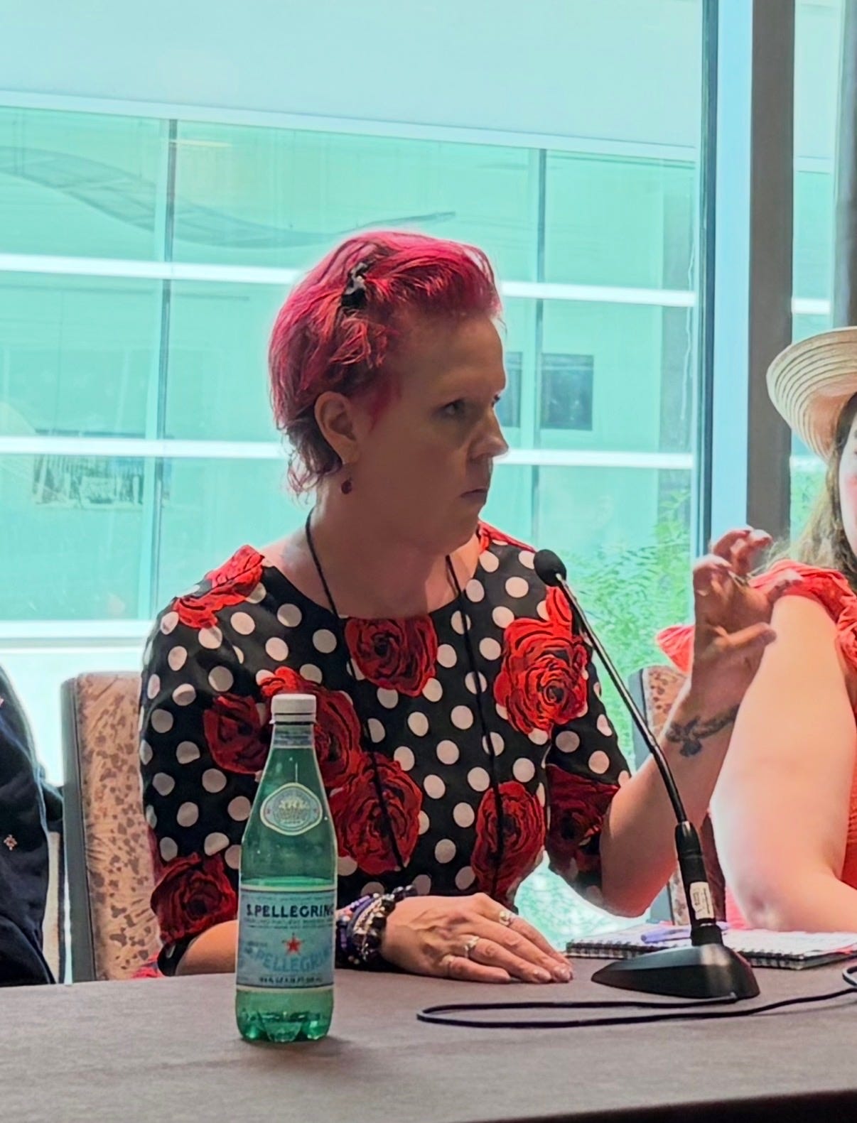 a woman with bright red hair and a dress with bright red flowers speaking