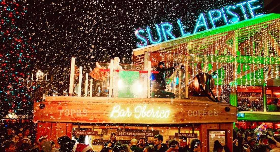 A night snowy scene with a wooden restaurant that says Bar Iberico in neon lights A night snowy scene with a wooden restaurant that says Bar Iberico in neon lights