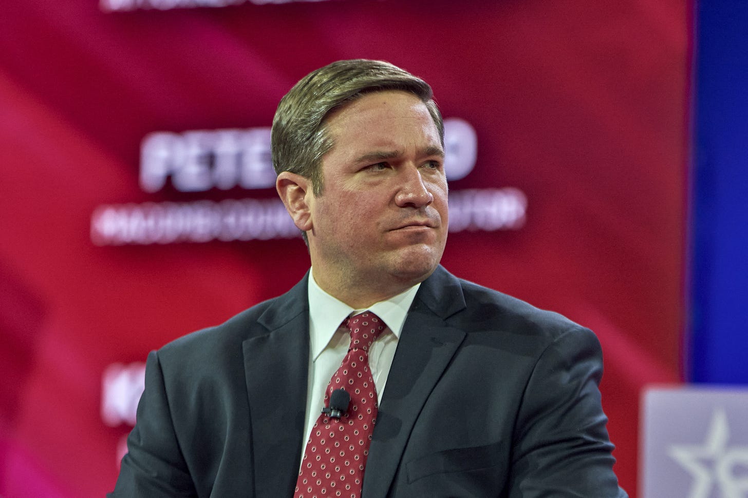 A middle-aged man, Missouri Attorney General Andrew Bailey, in a dark suit against a red background.