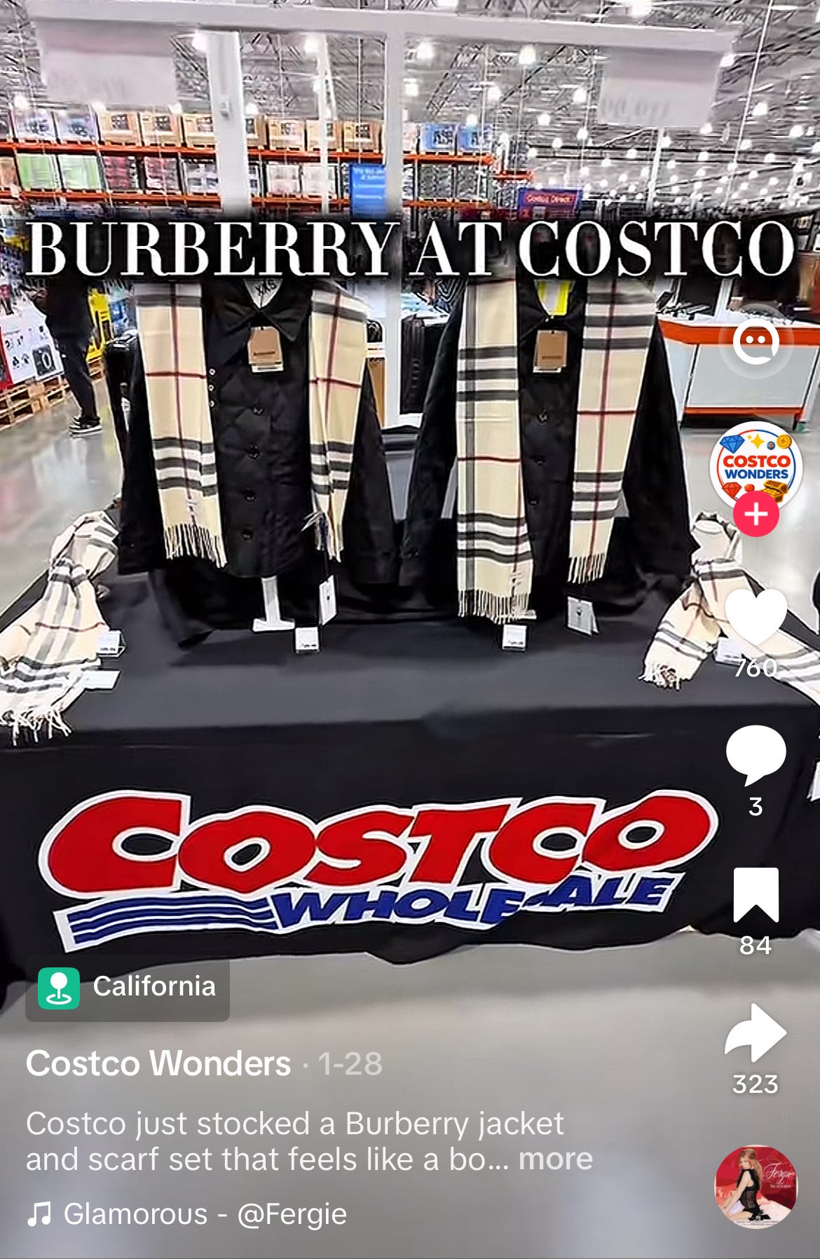TikTok screenshot from creator Costco Wonders dated January 28 and geo-tagged California, documenting a full Burberry merchandise activation at a US Costco Wholesale warehouse store. The image shows two mannequin-style display forms outfitted with Burberry black quilted outerwear and styled with the iconic Burberry check cashmere scarves in the signature camel, black, white, and red color palette, positioned on a black cloth-covered Costco merchandise table. Additional folded Burberry check scarves are arranged on both sides of the table, and individual price-sign cards are visible at the base of each display. The Costco Wholesale logo (red lettering with blue wave detailing and the "WHOLESALE" wordmark) is prominently displayed across the front of the table cloth, removing any ambiguity about the retail channel or whether this is an authorized or unauthorized distribution context. Behind the display, the warehouse's signature high-bay industrial racks stocked with palletized inventory, exposed steel-truss ceiling, and fluorescent overhead lighting are clearly visible. Bold white serif text overlay reads "BURBERRY AT COSTCO." The TikTok post caption reads "Costco just stocked a Burberry jacket and scarf set that feels like a [bonus/bargain]," and the video has 760 likes, 3 comments, 84 saves, and 323 shares, with a California location tag confirming US West Coast distribution. The styling of the jacket-and-scarf set as a coordinated outfit (rather than individual SKUs) suggests an intentional merchandising program rather than random parallel-import inventory, raising questions about whether Burberry has an active US wholesale agreement with Costco, whether this is liquidation through an authorized off-price channel partner, or whether this is gray-market parallel-import sourcing. Channel-check evidence material to Burberry $BRBY.L investors evaluating brand positioning discipline, distribution architecture, wholesale channel exposure, and the credibility of management's articulated heritage refocus narrative under CEO Joshua Schulman. The trench-and-scarf and quilted-jacket-and-scarf combinations being merchandised at Costco are precisely the hero category pairings the company cites as evidence of a successful return to heritage anchors.