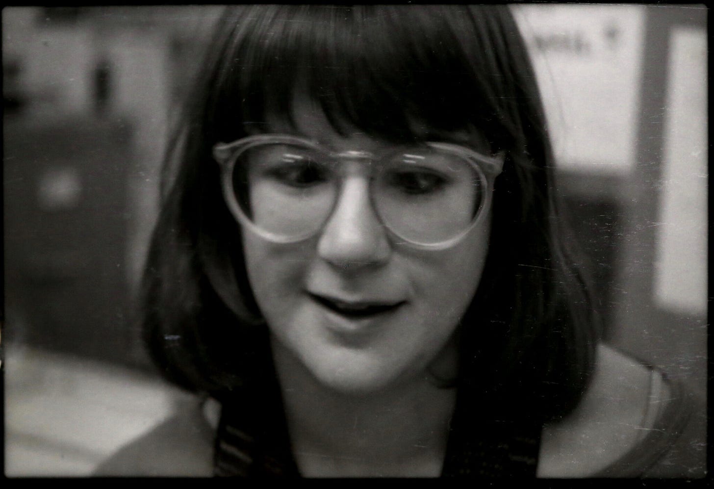 A black-and-white photo of a young, bespectacled woman with dark hair. Her lips are slightly parted as if she's in conversation.