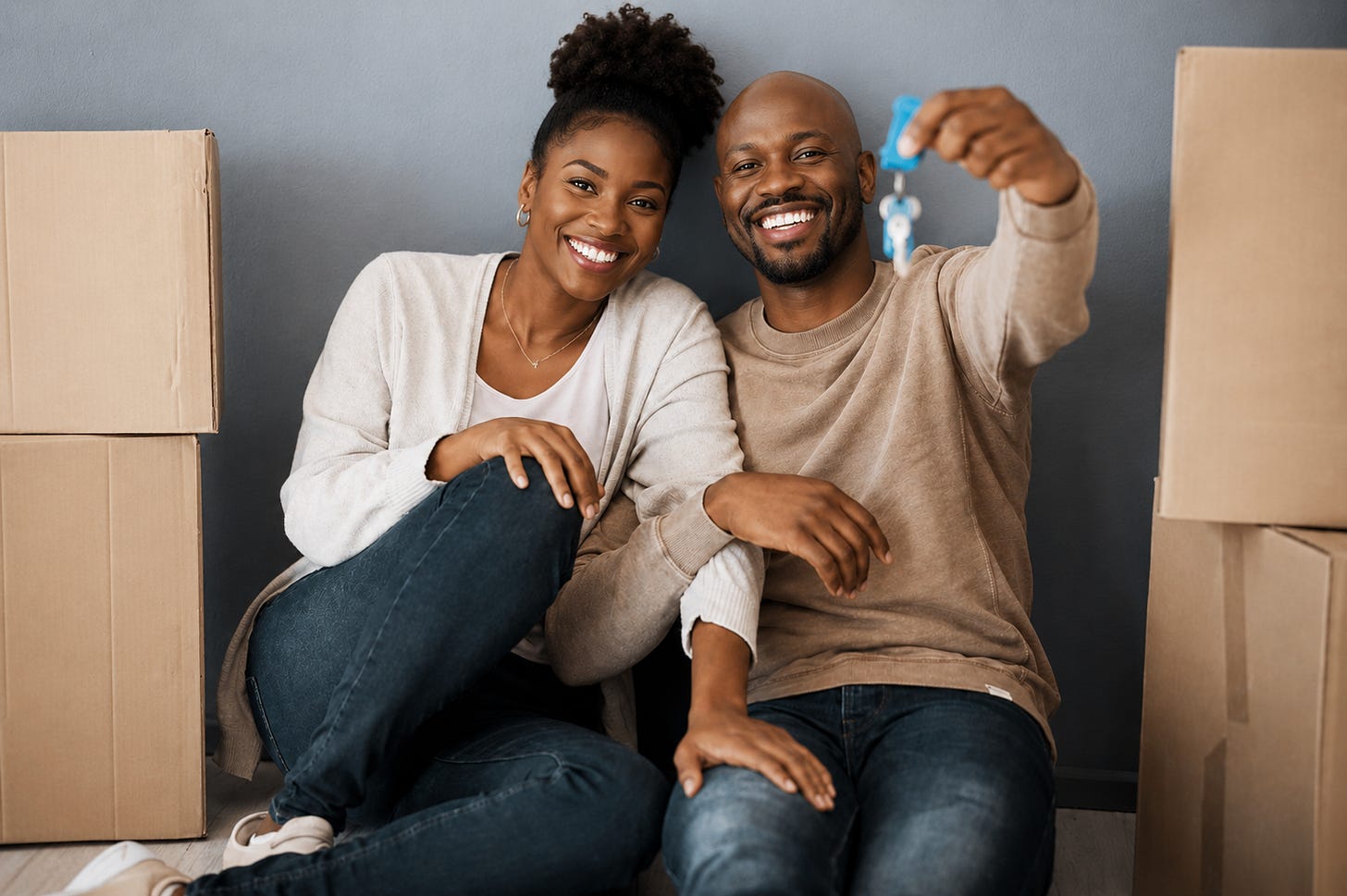 A young couple celebrates a major milestone as they sit among moving boxes in their new home, smiling while holding up the keys to a fresh beginning.