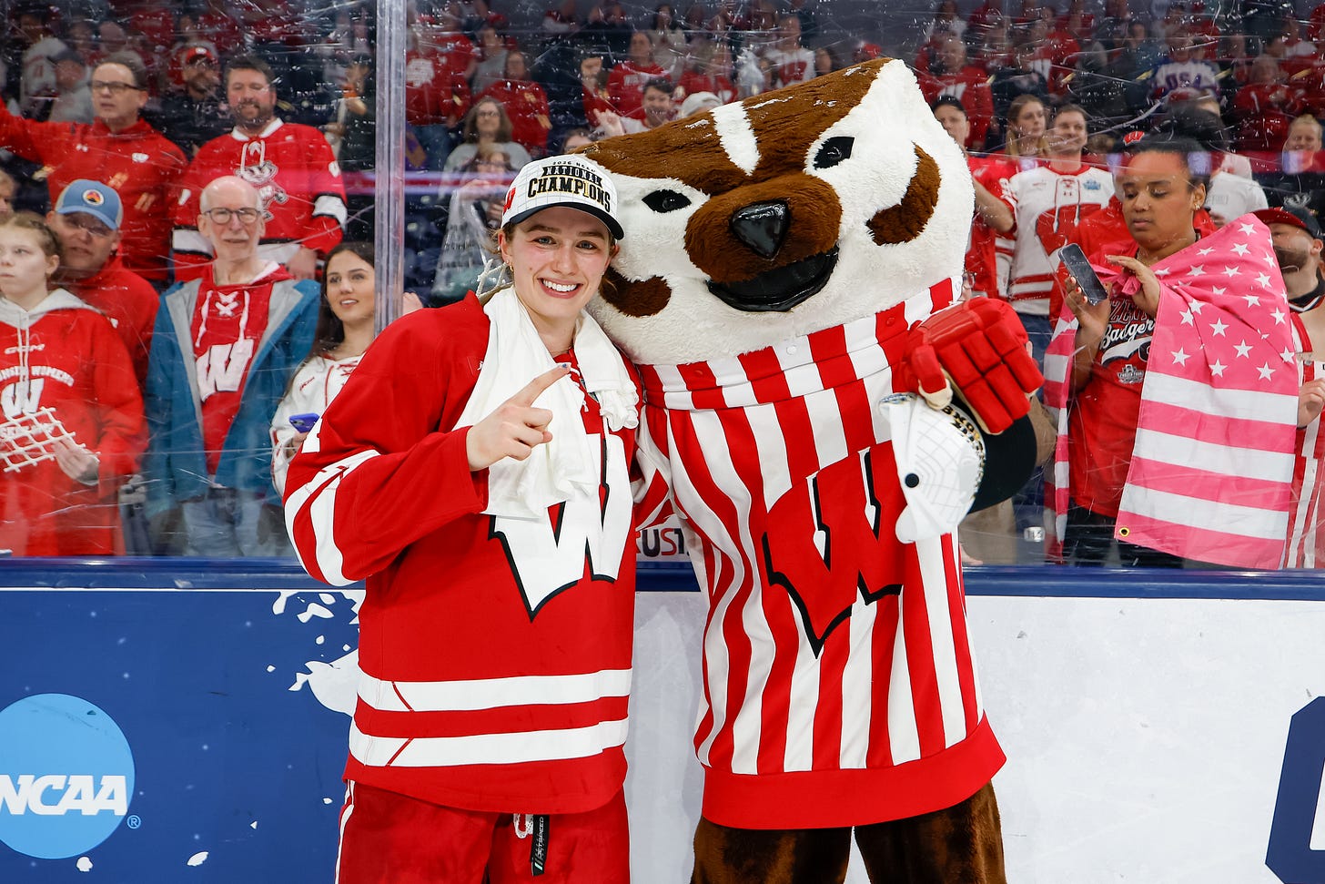 Caroline Harvey poses for a photo with Bucky Badger near the boards of the rink
