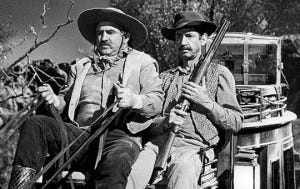 HAFF] The term "riding shotgun" originated in the old west, referring to  the person who rode alongside the "driver" of a stagecoach, whose job it  was to hold a shotgun and scare