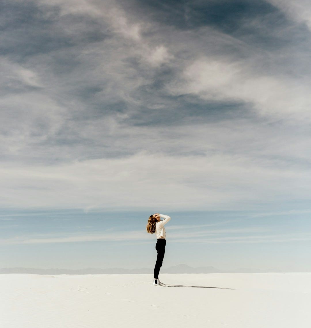 woman looking up to the sky while standing on white sand