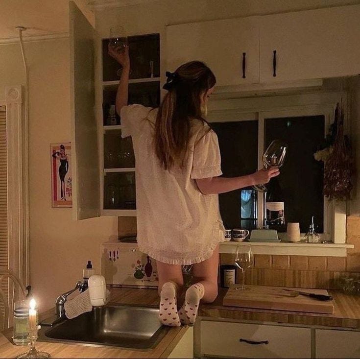 This may contain: a woman standing on top of a kitchen counter holding a wine glass in her hand