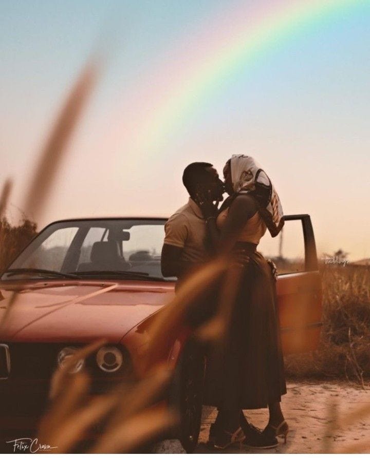 This may contain: a man and woman standing next to a car with a rainbow in the background