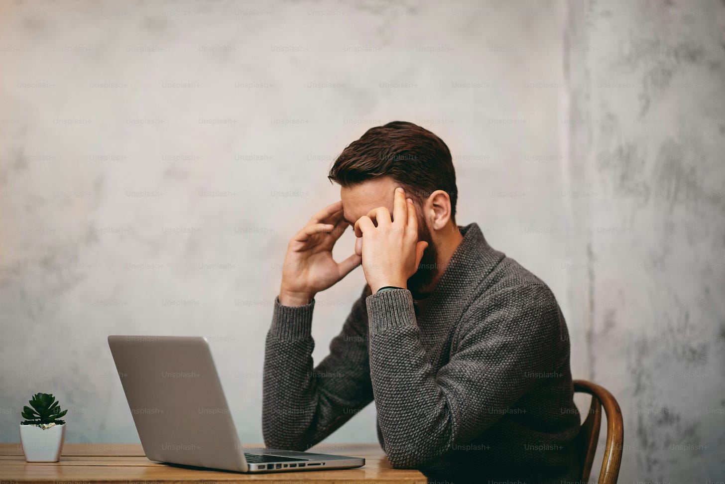 Man having headache while sitting in cafe. Laptop in front of him  and hands on head