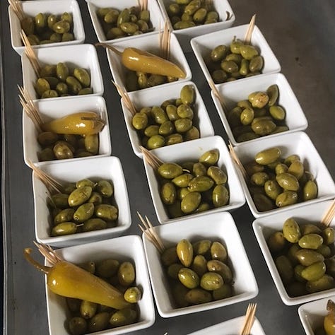 A poster for Falastin Film Festival saying 'sold out'; The room set for the Palestinian meal; Palestinian olives and chillies in small white bowls with cocktail sticks.