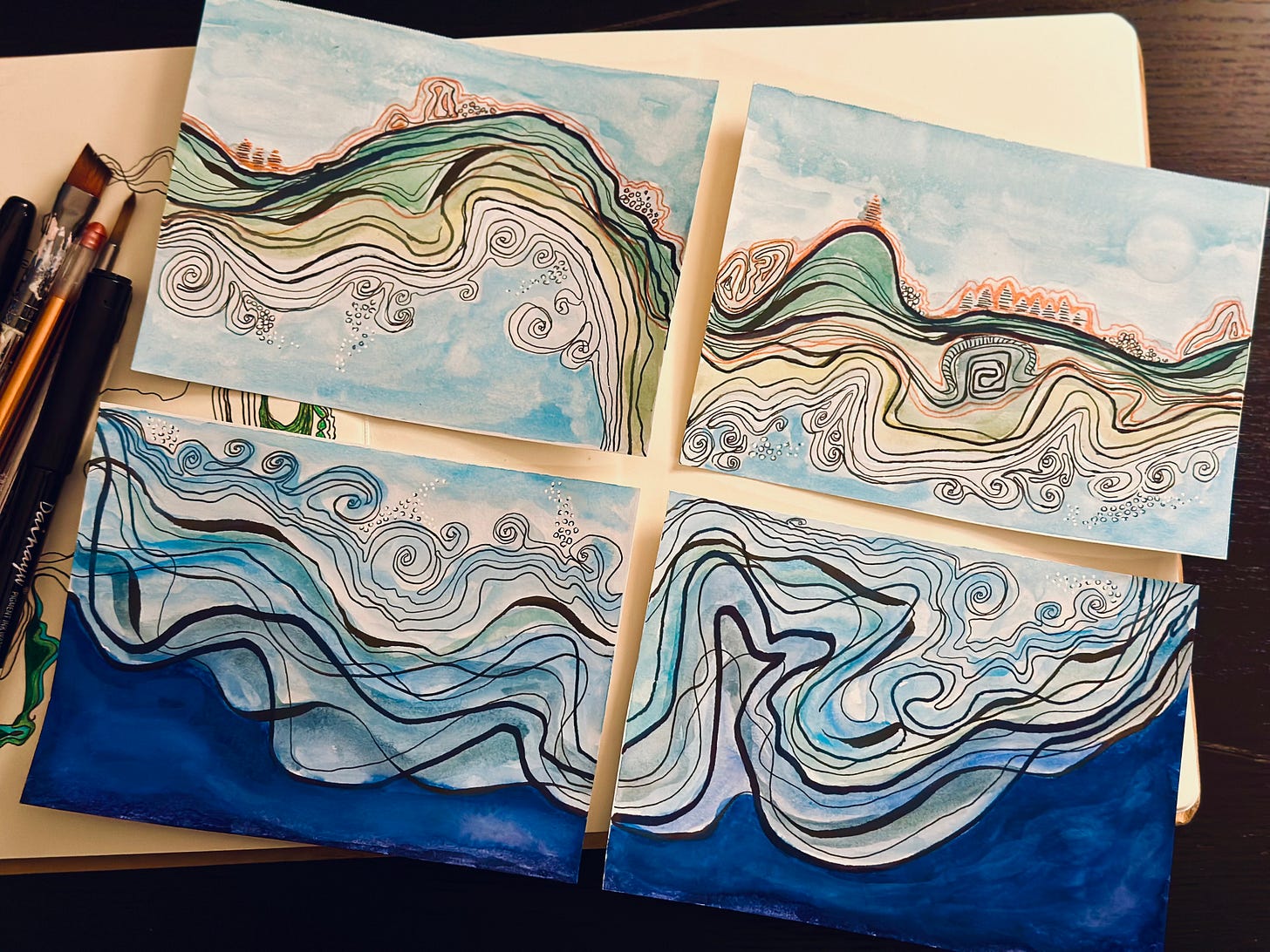 Four abstract pieces of art lay on a sketchbook with pens and paint brushes next to it. The art is made with varying widths of black lines making many shapes which imply land, beach and ocean. Watercolor fill in each with green, tan and blue. There are copper lines throughout. Together, the four pieces of art make one image but they have been cut in to four smaller pieces of art that are 4 by 6 inches each.  