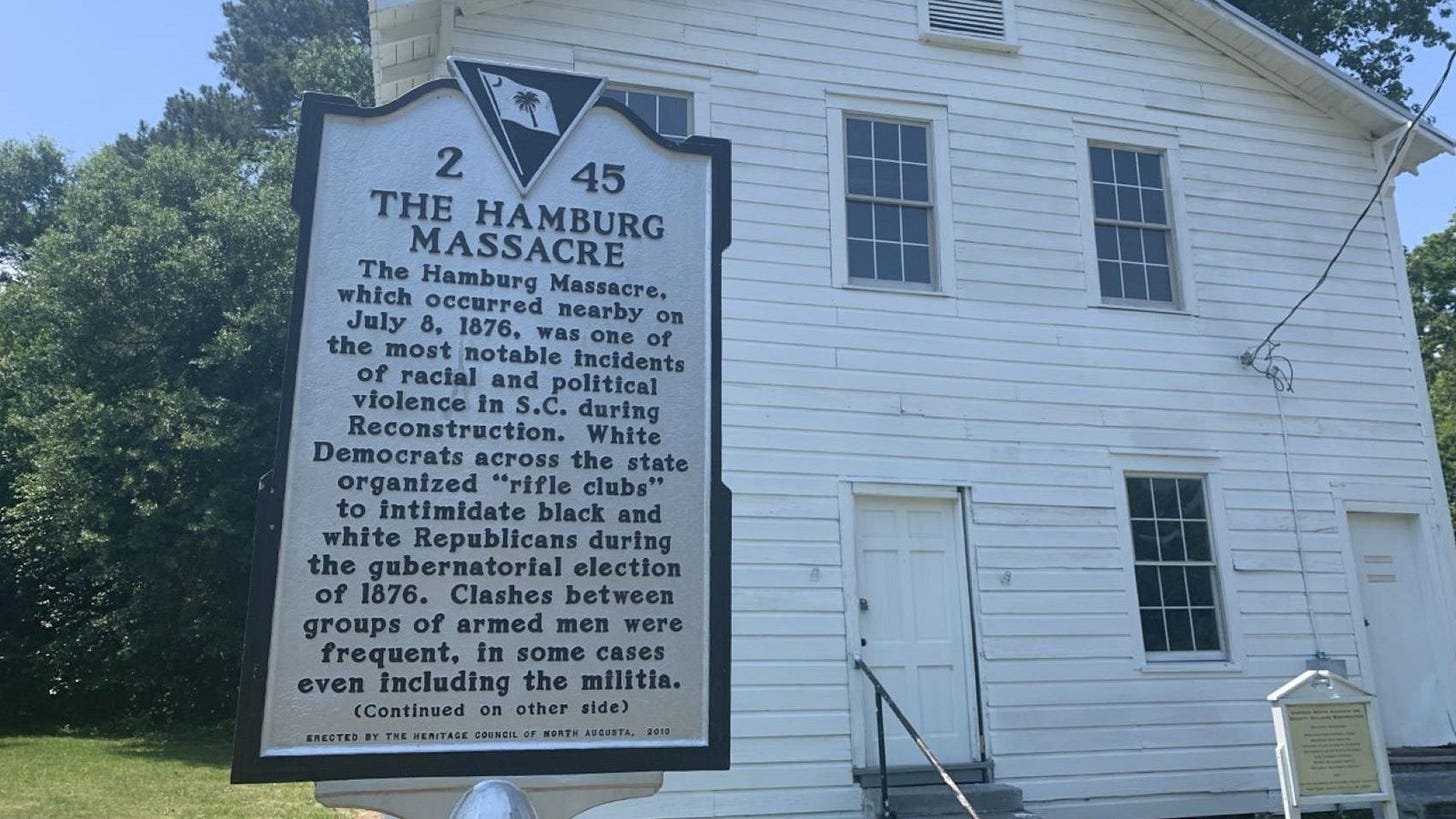 A white two-story building stands behind a white sign that reads A white two-story building stands behind a white sign that reads