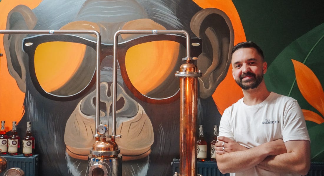 A man - Tom Axten, with an ape mural and copper distill behind him A man - Tom Axten, with an ape mural and copper distill behind him