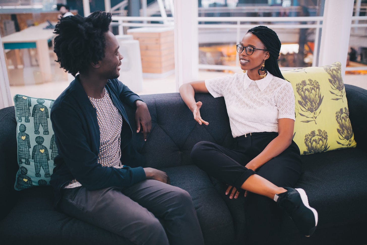 Two young adults talk to one another on the couch of a lobby.