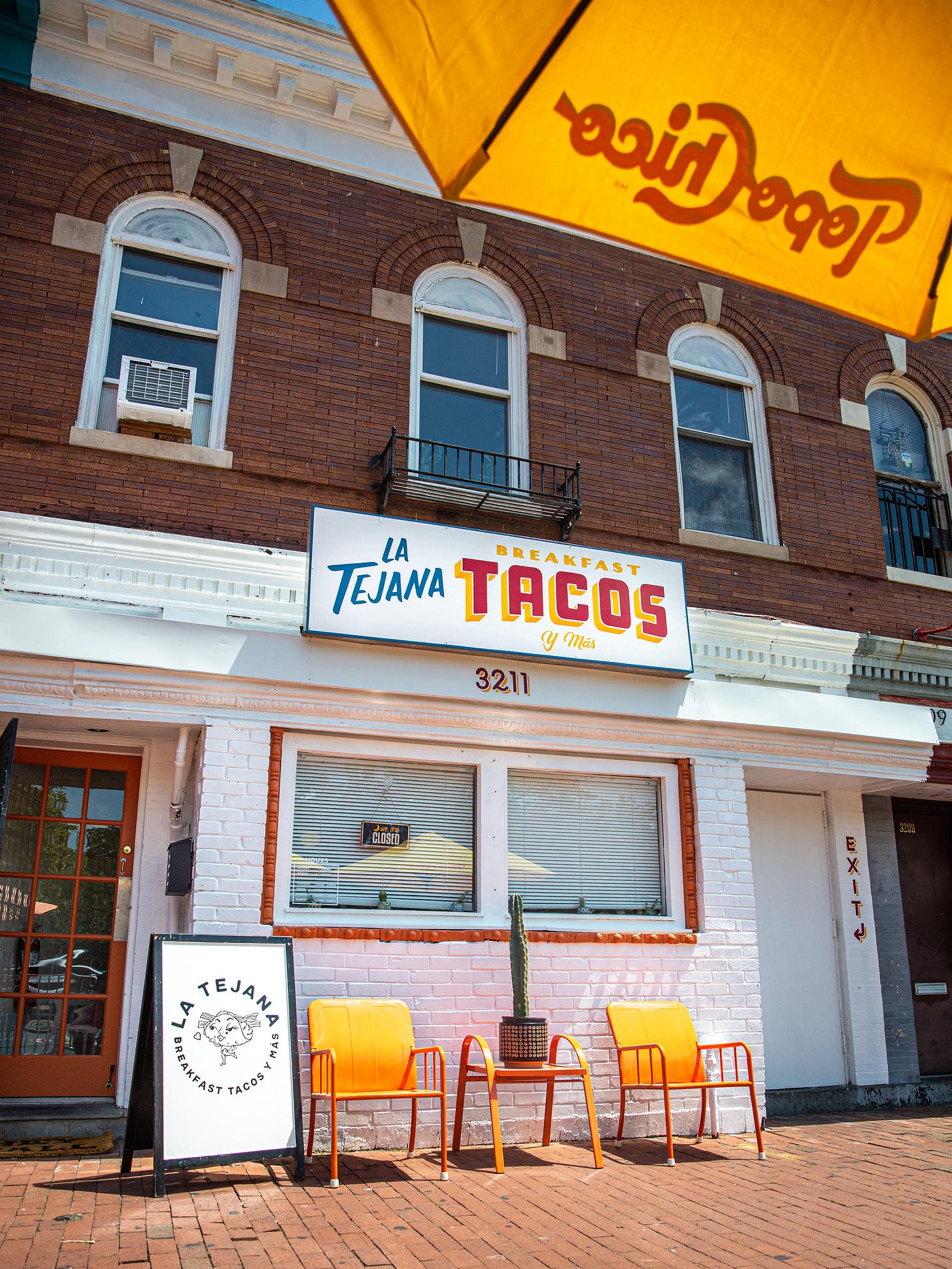 The exterior of La Tejana, with its white brick and orange patio furniture
