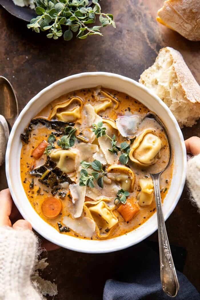 overhead photo of Healthier Slow Cooker Creamy Tortellini Vegetable Soup with 2 hands on bowl overhead photo of Healthier Slow Cooker Creamy Tortellini Vegetable Soup with 2 hands on bowl