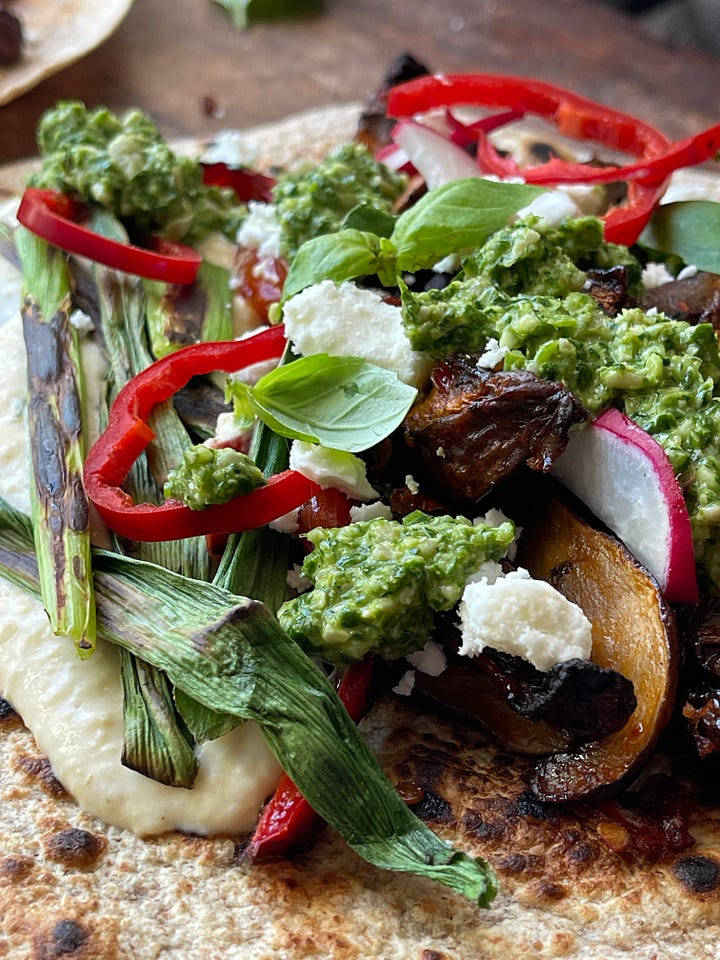 Overhead view of a roasted portobello mushroom wrap with pistachio basil pesto, sliced radishes, red pepper, crumbled feta, and fresh basil leaves on a charred wheat flatbread