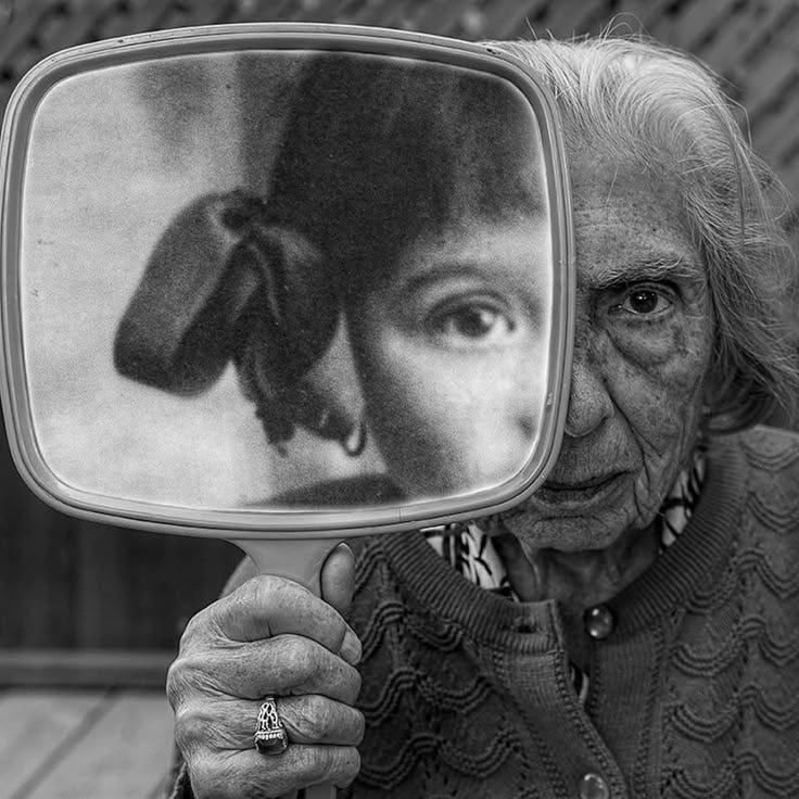 This may contain: an old woman is holding up a mirror to show her reflection in it's image