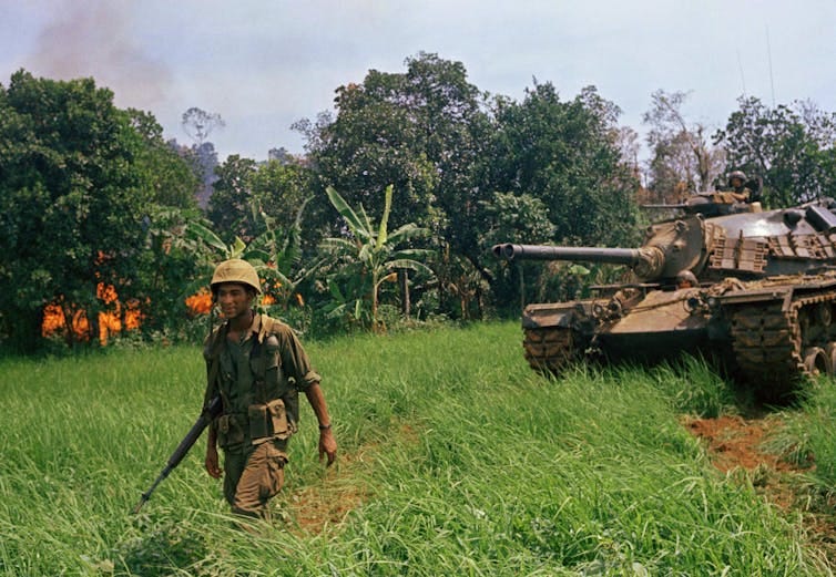 A tank and soldier pass by a burning area of forest. A tank and soldier pass by a burning area of forest.