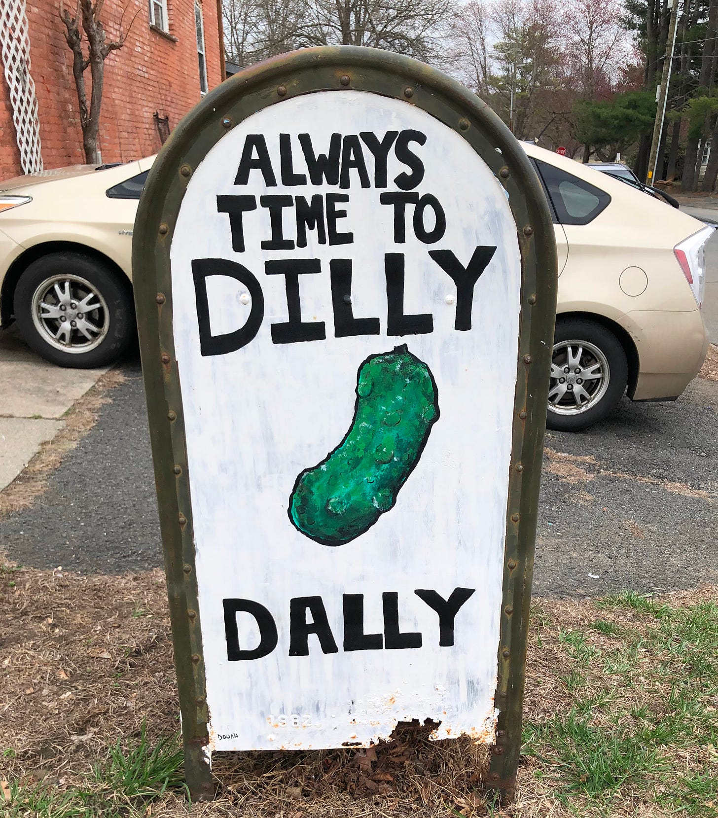 A decomissioned mailbox painted with the words "Always time to dilly dally" and an image of a dill pickle.