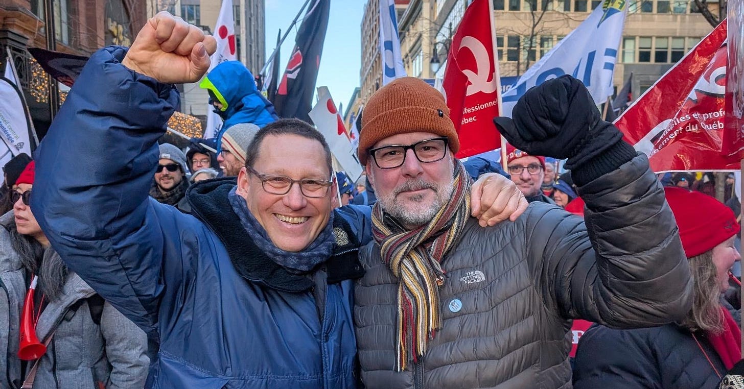 English: Avi Lewis and Alexandre Boulerice on the street at a protest in Montreal. They have their arms around eachother and both are holding up their fists. 

Français: Avi Lewis et Alexandre Boulerice dans la rue lors d'une manifestation à Montréal. Ils se tiennent par les épaules et lèvent tous deux le poing. 