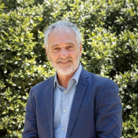 Portrait de Mendez Galain, cheveux blancs, courte barbe, sourire franc.