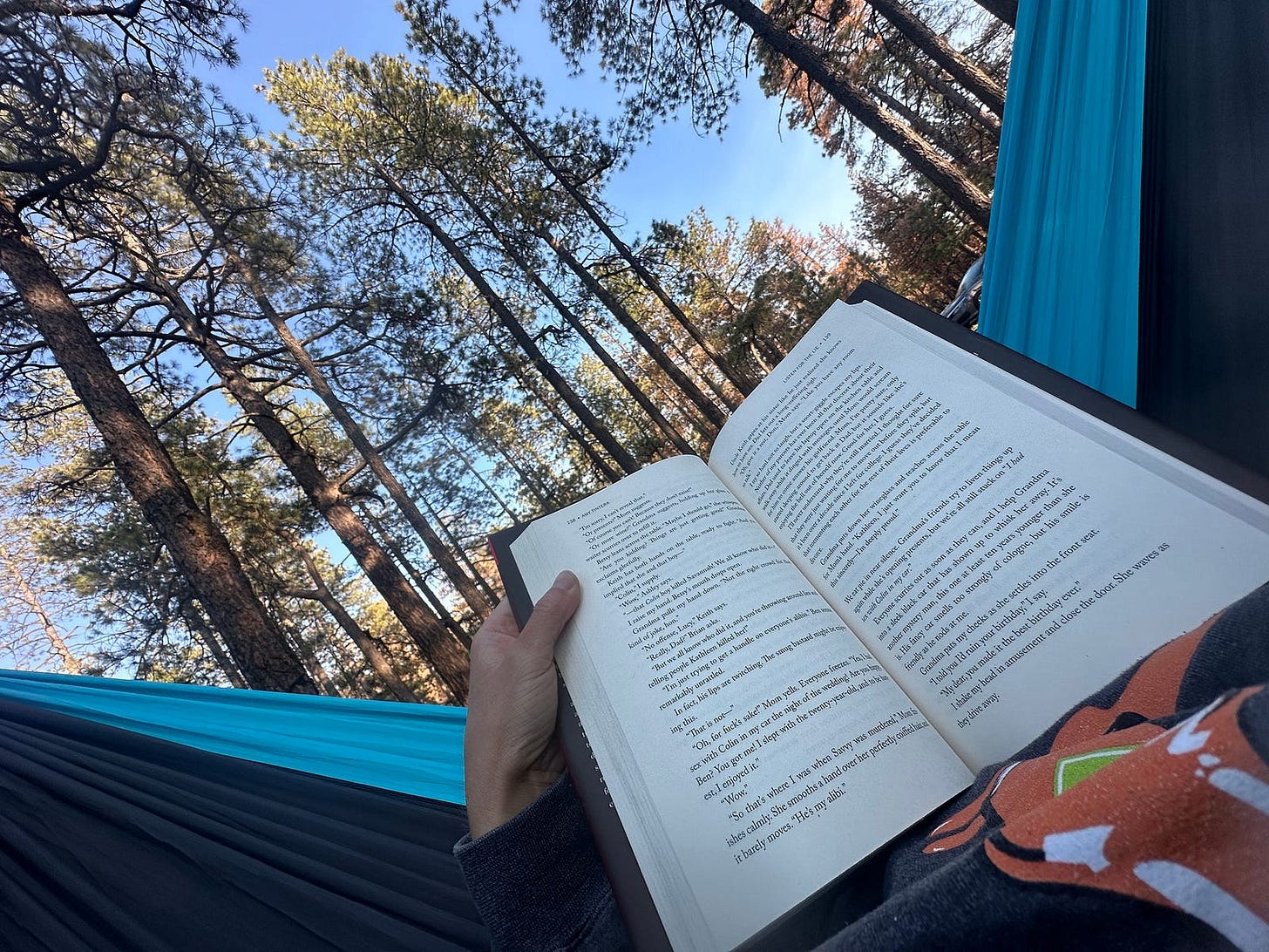 Woman laying in hammock in woods, holding an open book
