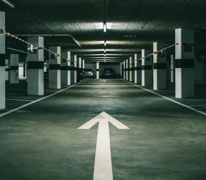 A darkened parking garage where a white arrow points forward along the path A darkened parking garage where a white arrow points forward along the path
