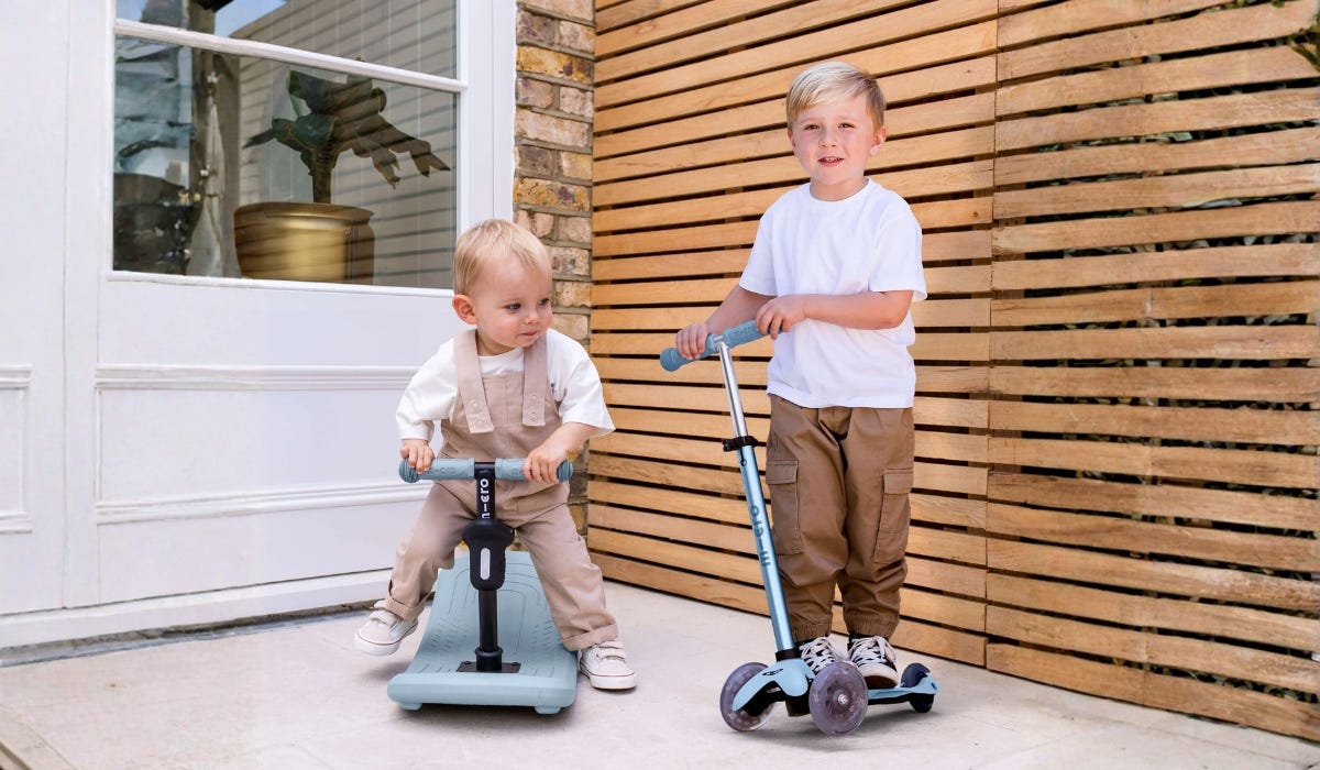 A toddler and young child on their scooters in a garden setting 