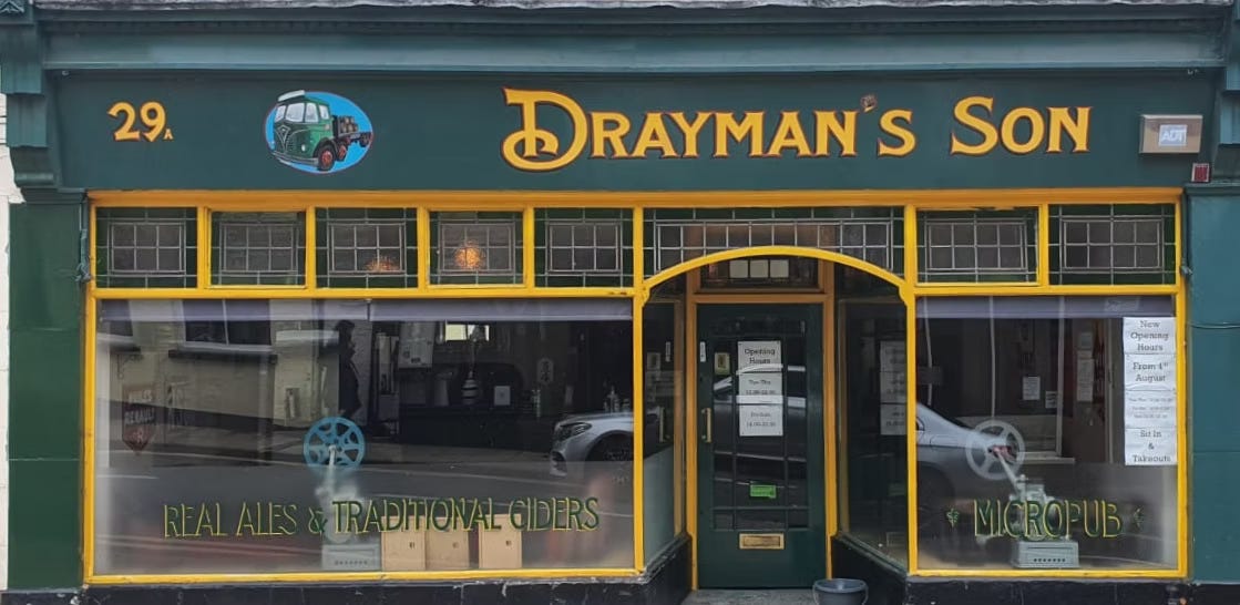 The outside of the pub, jaunty greens and yellows and original stained glass window detailing