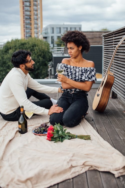 Free Man and Woman Sitting on Wooden Rooftop with Picnic Blanket Stock Photo