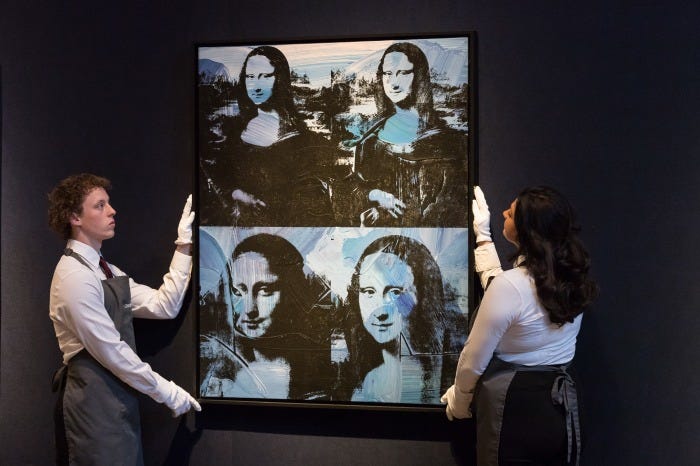 Two art handlers in white gloves hold up Andy Warhol's "Four Mona Lisas" painting.