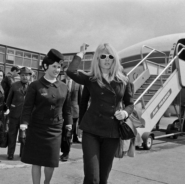 This may contain: black and white photo of two women in uniforms walking towards an airplane with people standing around