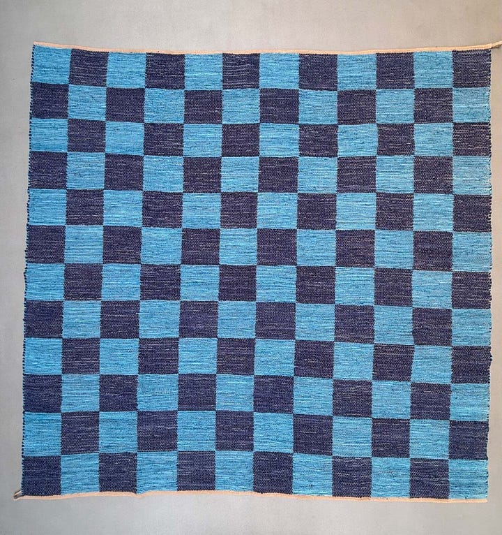 a chequerboard blue rug, a blue and red striped cushion