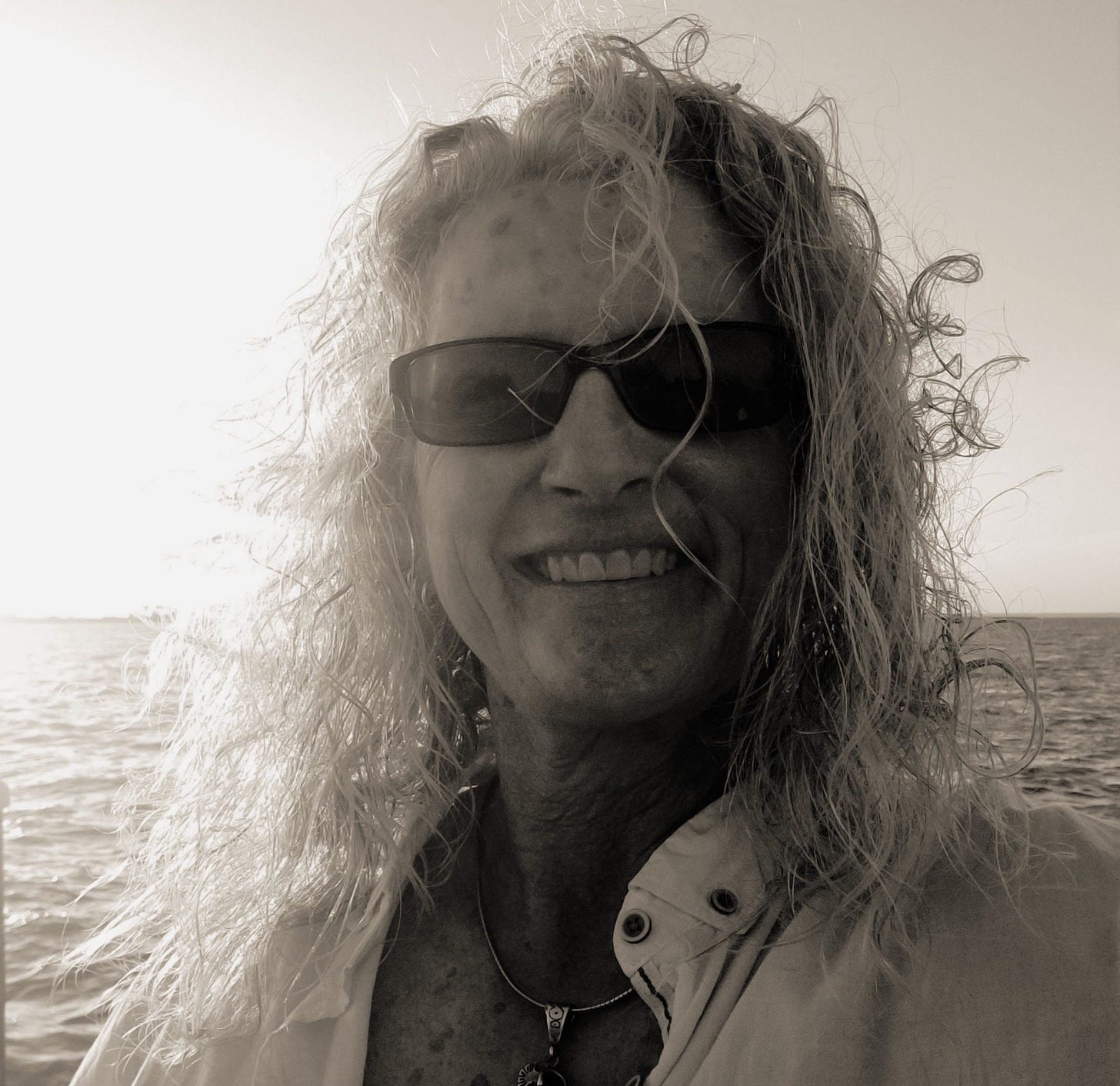 Guest poster Janice Anne Wheeler, hair flying in the wind, sunlit ocean behind her