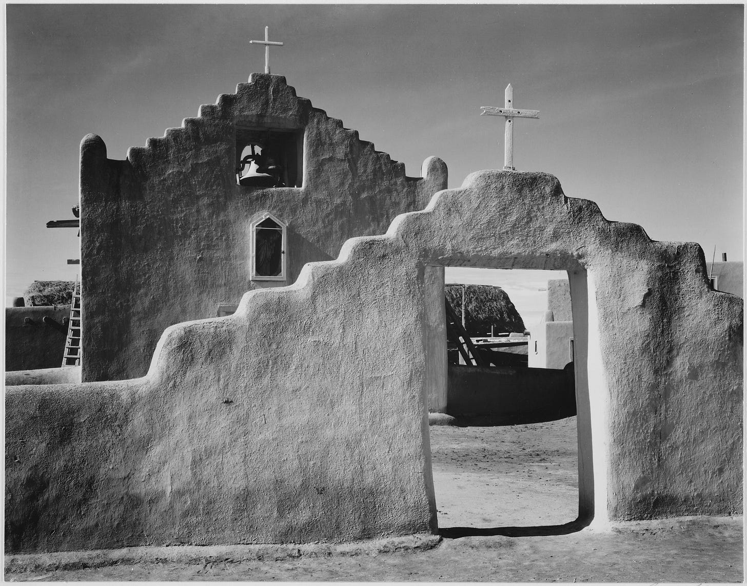 Ansel Adams, Public domain, via Wikimedia Commons: Full side view of entrance with gate to the right, "Church, Taos Pueblo National Historic Landmark, New Mexico, 1941." [Misicn de San Gercnimo]; From the series Ansel Adams Photographs of National Parks and Monuments, compiled 1941 - 1942, documenting the period ca. 1933 - 1942.