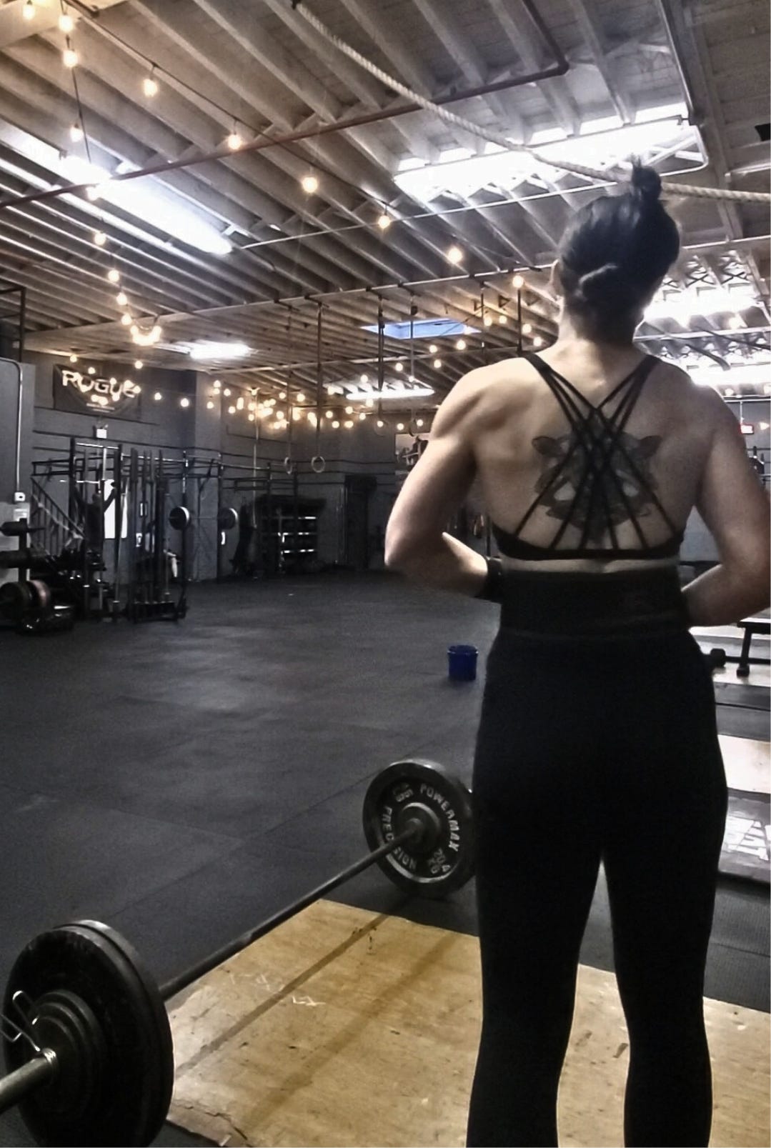 Author stands with their back to camera, tightening their lifting belt. a barbell with weights on it sits on the ground to their left.