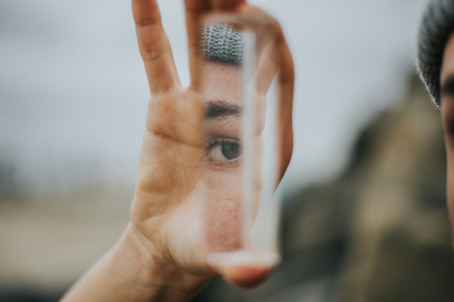 Photo of a hand holding up a glass cube in which their eye can be seen reflected.