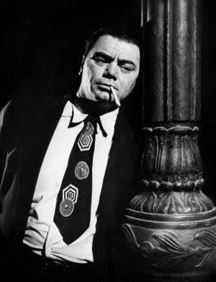Still image in black and white from the movie Marty showing Ernest Borgnine portraying the title character. He's leaning against a pillar with a cigarette in his mouth.