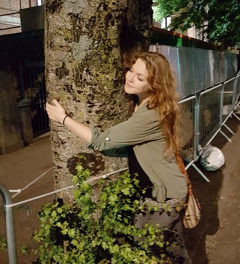 A young child and a woman hugs a tree.
