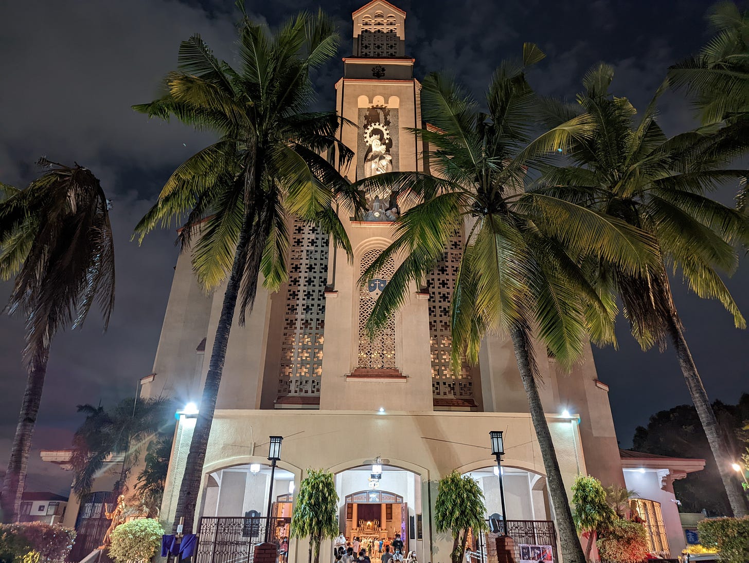 The exterior of Our Lady of Mount Carmel showing the tall trees of the parking lot