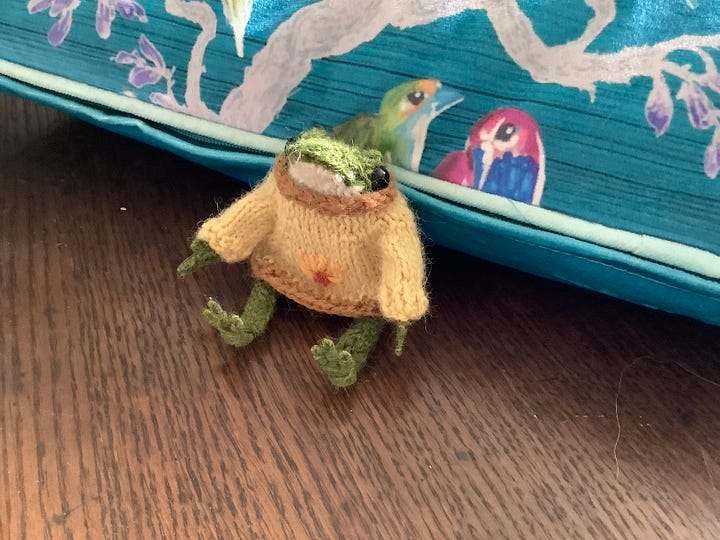 A tiny knitted frog in a cream jumper in a variety of poses, one without the jumpers and looking balletic