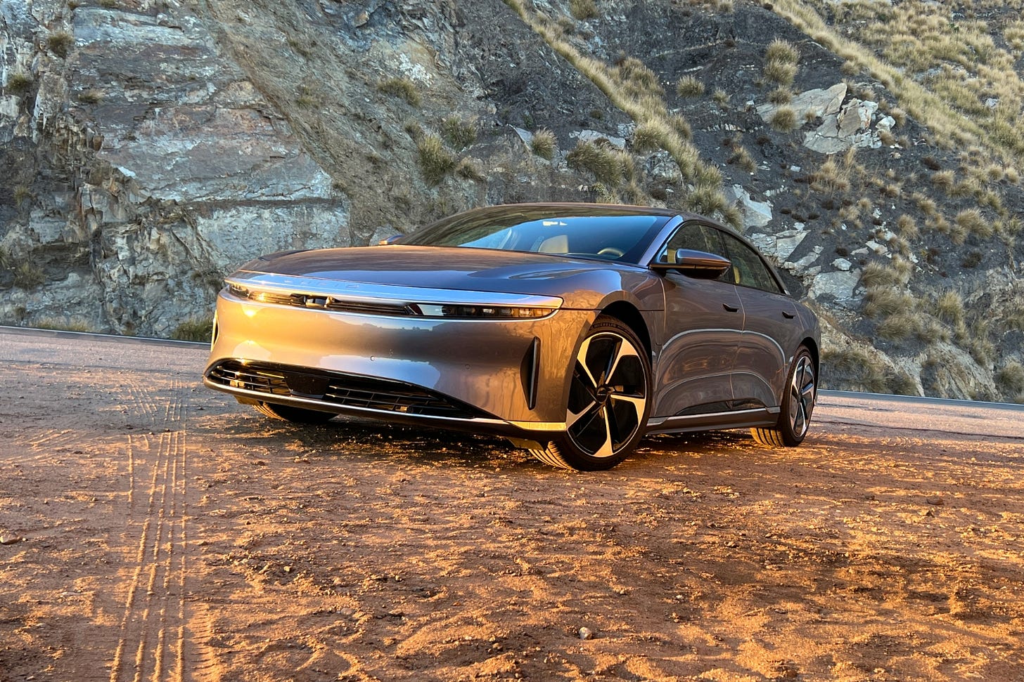 A gray 2023 Lucid Air Pure is parked on sand at sunset.
