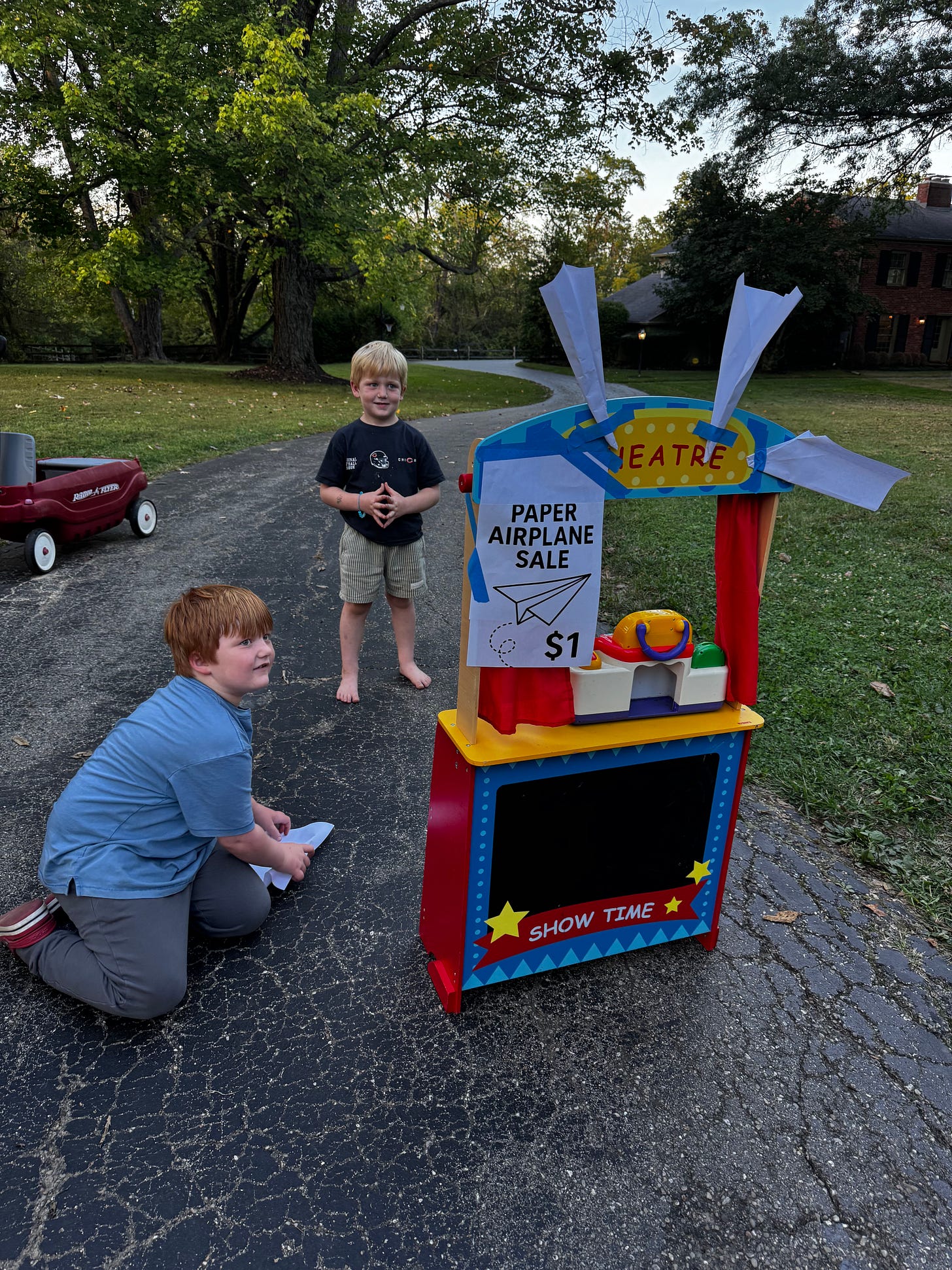 Young boy selling handmade paper airplanes from a driveway stand, symbolizing creativity, hustle, and early entrepreneurship.