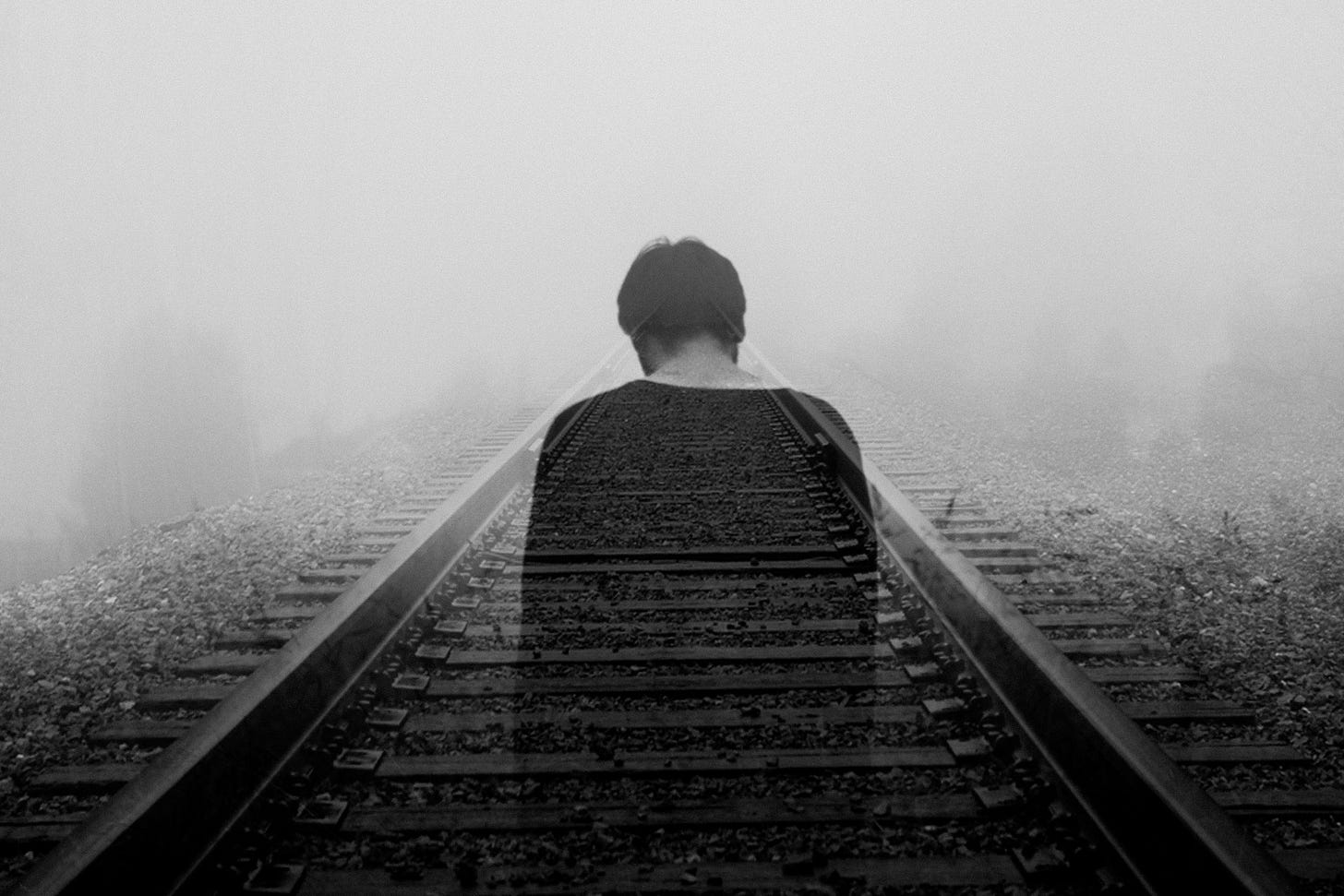 A greyscale image of a lone man on a train track. The man is translucent and ghostly.