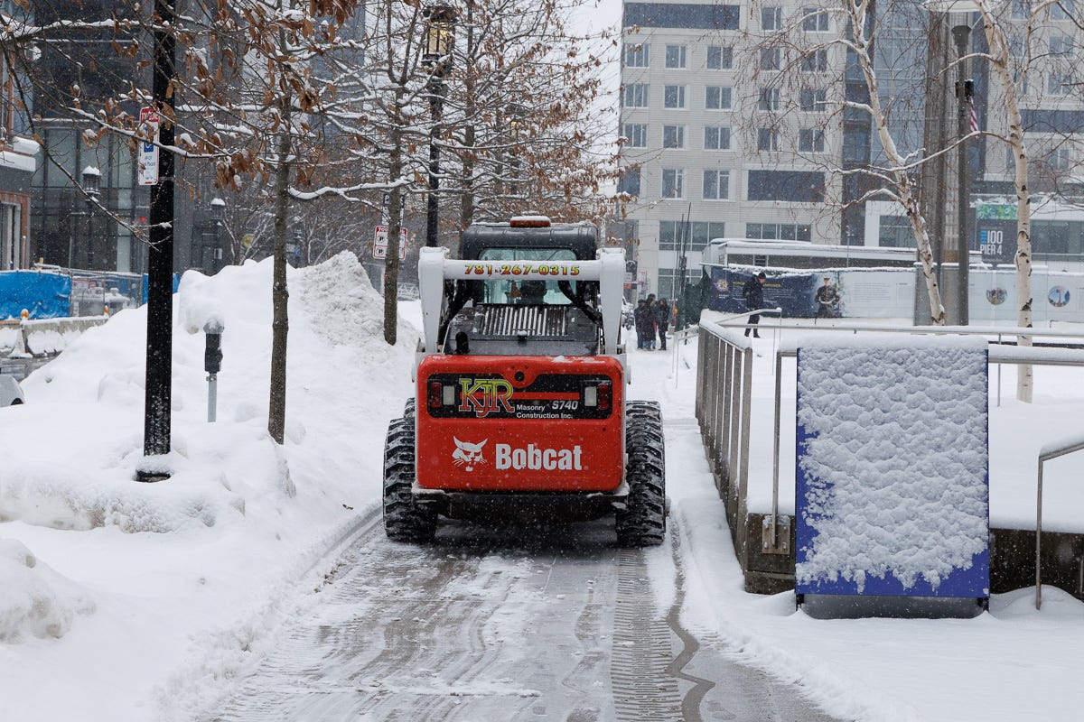 Bobcat loader clearing a narrow pedestrian path between snowbanks in Boston Seaport.