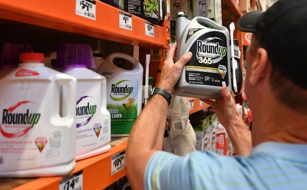 A man holds up a container of Roundup in a pesticide aisle at a store.